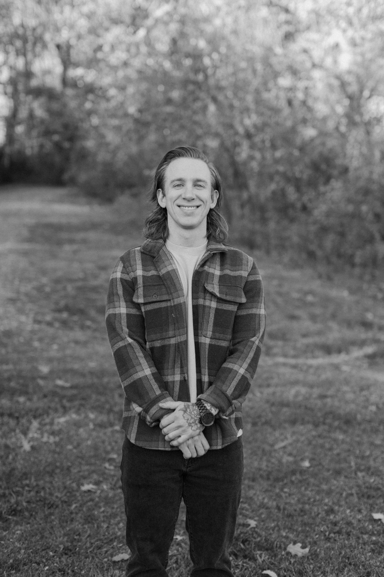 Evan Reynolds smiling outdoors in a plaid overshirt, in black and white.